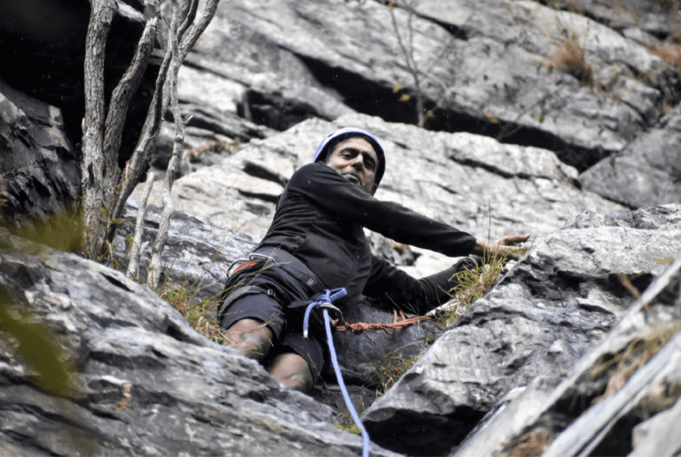 Proud rock climber looks down with a smile at his achievements.